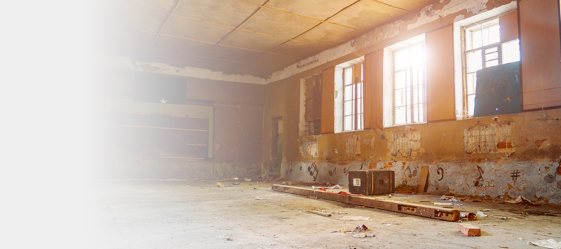 Interior commercial space with exposed ceiling, walls and subfloor, littered with garbage.